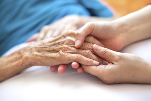 Holding elderly person's hand in bed